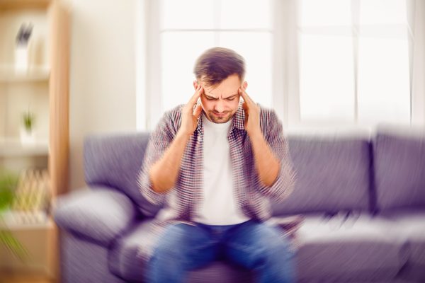 Man suddenly feels dizzy and takes a seat on the sofa. Young guy feeling pain and spinning sensation in his head. Headache, vertigo, health problem, brain tumor concept